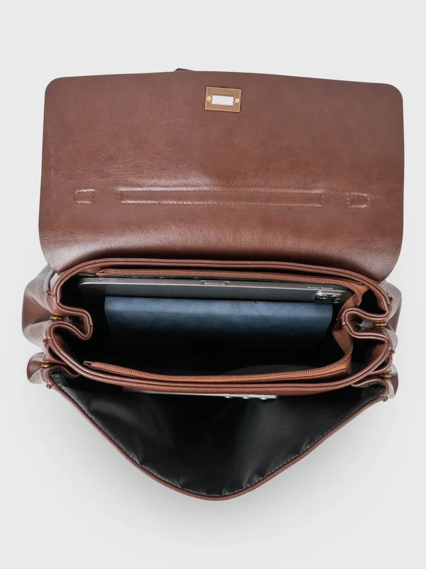 Brown leather shoulder bag with structured shape, flap closure and slim top handle, photographed on a light background