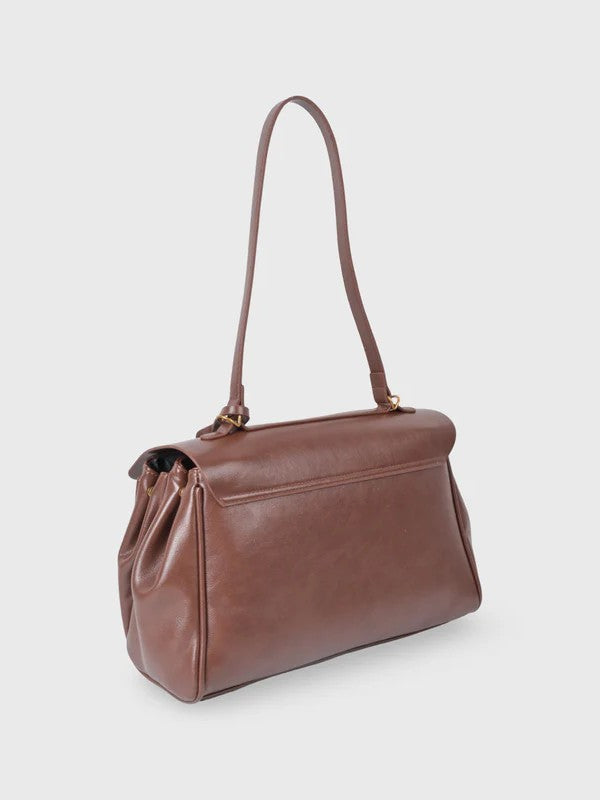 Brown leather shoulder bag with structured shape, flap closure and slim top handle, photographed on a light background