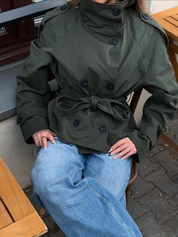 trench coat for women with a structured fit, high collar and dark buttons. Crafted from premium fabric, it highlights the waist and adds refined elegance to any autumn or winter outfit.