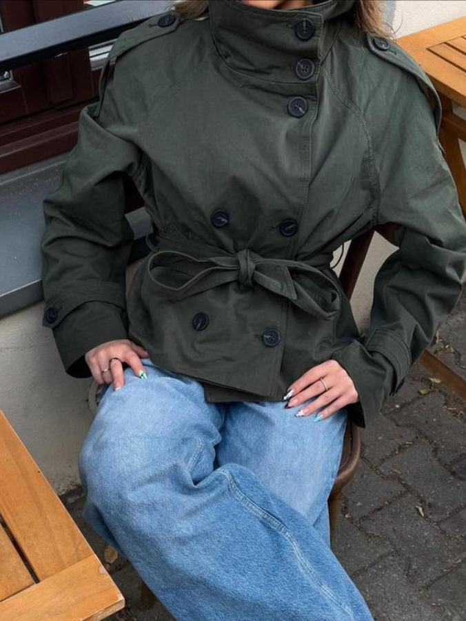 trench coat for women with a structured fit, high collar and dark buttons. Crafted from premium fabric, it highlights the waist and adds refined elegance to any autumn or winter outfit.