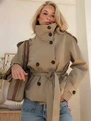trench coat for women with a structured fit, high collar and dark buttons. Crafted from premium fabric, it highlights the waist and adds refined elegance to any autumn or winter outfit.