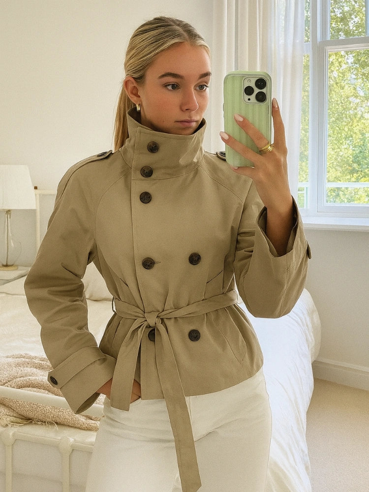 trench coat for women with a structured fit, high collar and dark buttons. Crafted from premium fabric, it highlights the waist and adds refined elegance to any autumn or winter outfit.