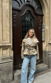 trench coat for women with a structured fit, high collar and dark buttons. Crafted from premium fabric, it highlights the waist and adds refined elegance to any autumn or winter outfit.