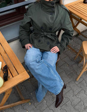 trench coat for women with a structured fit, high collar and dark buttons. Crafted from premium fabric, it highlights the waist and adds refined elegance to any autumn or winter outfit.