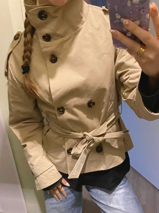 trench coat for women with a structured fit, high collar and dark buttons. Crafted from premium fabric, it highlights the waist and adds refined elegance to any autumn or winter outfit.