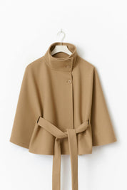 High-Neck Belted Cape Jacket in camel wool blend. Poncho-inspired autumn/winter coat with high-neck collar, cape silhouette and adjustable waist belt. A chic belted jacket combining elegance, comfort and versatile seasonal style.