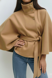 High-Neck Belted Cape Jacket in camel wool blend. Poncho-inspired autumn/winter coat with high-neck collar, cape silhouette and adjustable waist belt. A chic belted jacket combining elegance, comfort and versatile seasonal style.