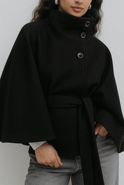 High-Neck Belted Cape Jacket in camel wool blend. Poncho-inspired autumn/winter coat with high-neck collar, cape silhouette and adjustable waist belt. A chic belted jacket combining elegance, comfort and versatile seasonal style.