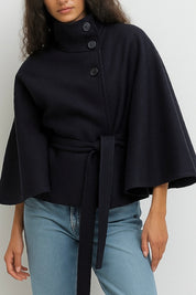 High-Neck Belted Cape Jacket in camel wool blend. Poncho-inspired autumn/winter coat with high-neck collar, cape silhouette and adjustable waist belt. A chic belted jacket combining elegance, comfort and versatile seasonal style.