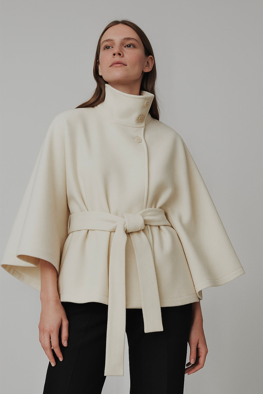 High-Neck Belted Cape Jacket in camel wool blend. Poncho-inspired autumn/winter coat with high-neck collar, cape silhouette and adjustable waist belt. A chic belted jacket combining elegance, comfort and versatile seasonal style.
