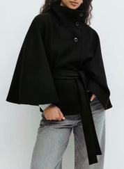 High-Neck Belted Cape Jacket in camel wool blend. Poncho-inspired autumn/winter coat with high-neck collar, cape silhouette and adjustable waist belt. A chic belted jacket combining elegance, comfort and versatile seasonal style.