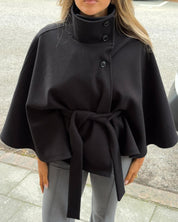 High-Neck Belted Cape Jacket in camel wool blend. Poncho-inspired autumn/winter coat with high-neck collar, cape silhouette and adjustable waist belt. A chic belted jacket combining elegance, comfort and versatile seasonal style.