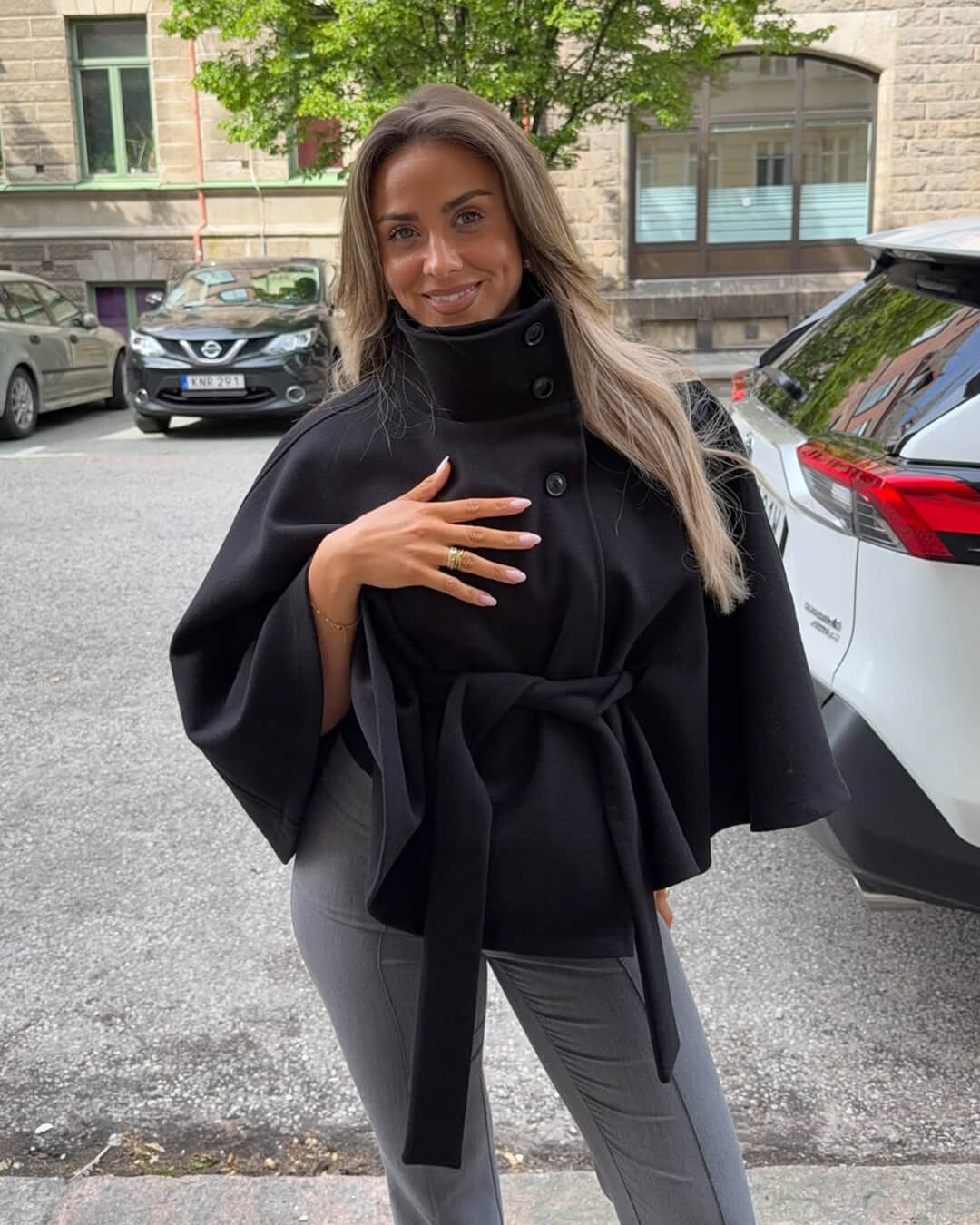 High-Neck Belted Cape Jacket in camel wool blend. Poncho-inspired autumn/winter coat with high-neck collar, cape silhouette and adjustable waist belt. A chic belted jacket combining elegance, comfort and versatile seasonal style.