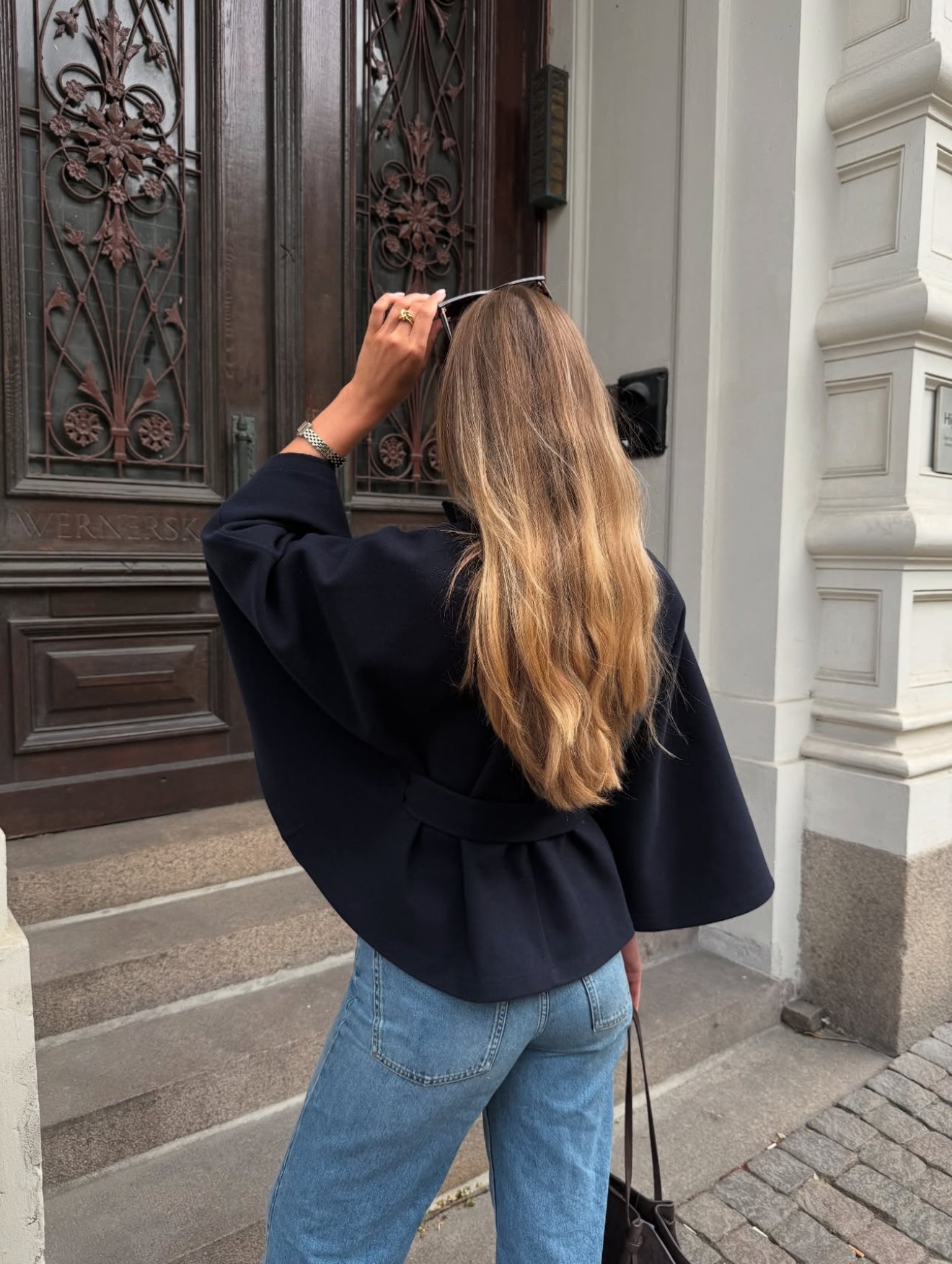 High-Neck Belted Cape Jacket in camel wool blend. Poncho-inspired autumn/winter coat with high-neck collar, cape silhouette and adjustable waist belt. A chic belted jacket combining elegance, comfort and versatile seasonal style.