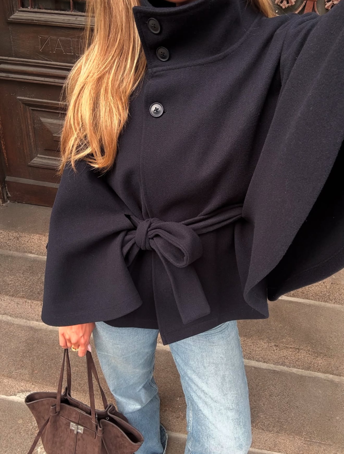 High-Neck Belted Cape Jacket in camel wool blend. Poncho-inspired autumn/winter coat with high-neck collar, cape silhouette and adjustable waist belt. A chic belted jacket combining elegance, comfort and versatile seasonal style.