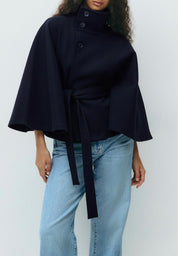 High-Neck Belted Cape Jacket in camel wool blend. Poncho-inspired autumn/winter coat with high-neck collar, cape silhouette and adjustable waist belt. A chic belted jacket combining elegance, comfort and versatile seasonal style.