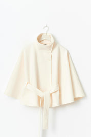 High-Neck Belted Cape Jacket in camel wool blend. Poncho-inspired autumn/winter coat with high-neck collar, cape silhouette and adjustable waist belt. A chic belted jacket combining elegance, comfort and versatile seasonal style.