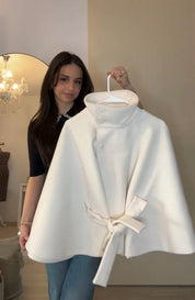 High-Neck Belted Cape Jacket in camel wool blend. Poncho-inspired autumn/winter coat with high-neck collar, cape silhouette and adjustable waist belt. A chic belted jacket combining elegance, comfort and versatile seasonal style.