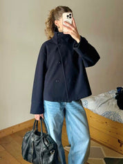 Black high-neck jacket with asymmetrical buttons and structured silhouette, featuring wide sleeves and a minimalist design for modern everyday styling.