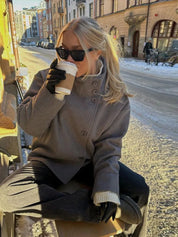 Black high-neck jacket with asymmetrical buttons and structured silhouette, featuring wide sleeves and a minimalist design for modern everyday styling.