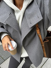 Black high-neck jacket with asymmetrical buttons and structured silhouette, featuring wide sleeves and a minimalist design for modern everyday styling.