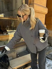 Black high-neck jacket with asymmetrical buttons and structured silhouette, featuring wide sleeves and a minimalist design for modern everyday styling.